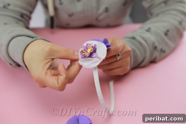 A handmade fabric flower being carefully positioned and hot-glued onto a plastic headband, demonstrating the final assembly step.