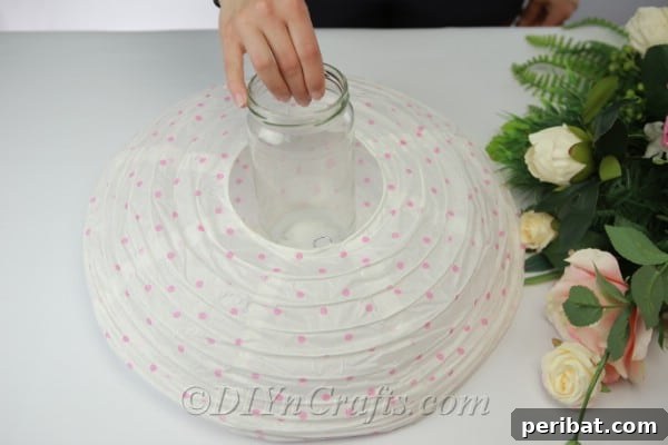 Measuring an empty glass jar against a collapsed paper lantern to ensure it's the correct height.