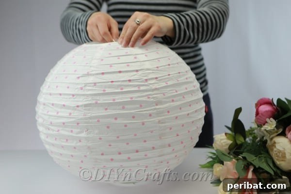 A paper lantern being pulled up and secured around a glass jar, demonstrating how the jar provides internal support.