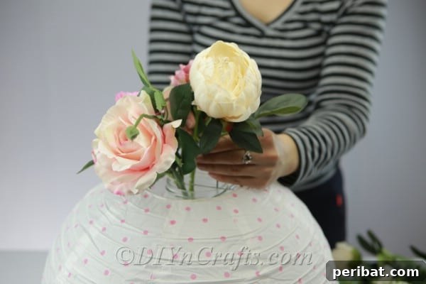 Close-up of hands arranging a colorful assortment of artificial flowers into the glass jar inside the paper lantern.