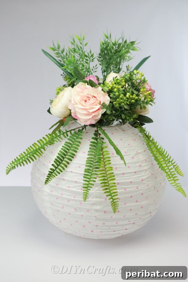 The finished paper lantern centerpiece, elegantly arranged with flowers and greenery, displayed on a surface.