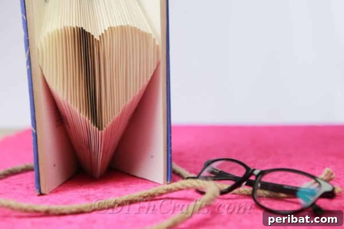 A beautifully folded book heart resting beside a pair of reading glasses, suggesting a thoughtful, creative activity.