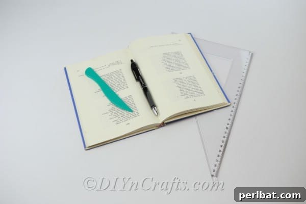 Supplies needed for book page folding art, including a hardback book, ruler, and pencil.