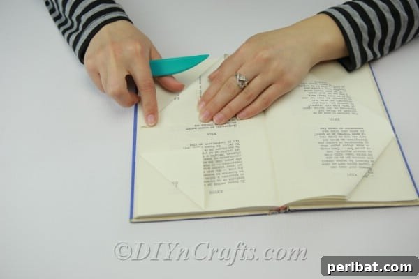 Showing the second fold, folding down the bottom corner of the book page to the second mark.
