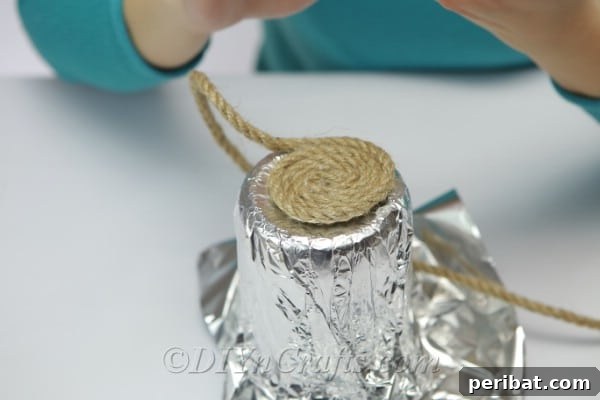 DIY Rope Baskets Elevate Your Storage Style 9 Diligently wrapping rope around a foil-covered jar, applying hot glue to secure each coil.