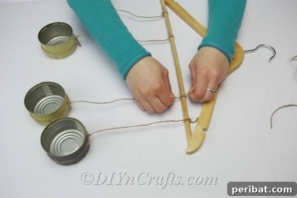 Transform Tuna Cans into Pretty Tealight Holders 10 Hanging tuna cans from a wooden clothes hanger with twine, illustrating varied lengths.
