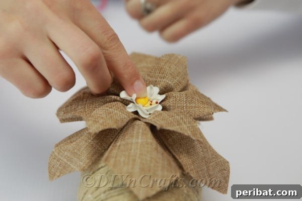 Gluing a small artificial flower to the center of a burlap ribbon flower on the vase, adding a refined decorative touch.