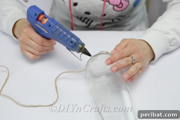 Starting to glue and wrap twine onto the bottom edge of a clean glass bottle, ensuring a snug and even start.