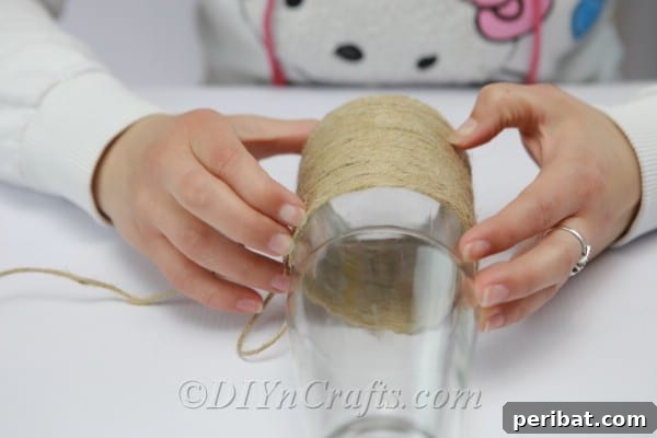 Wrapping and gluing twine systematically up a glass bottle, ensuring each coil is tight and evenly spaced.