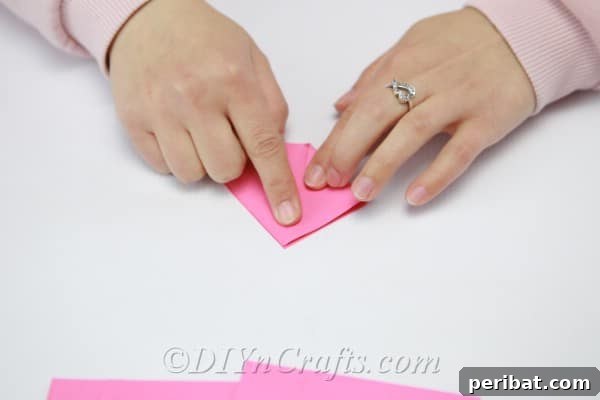 Pink paper triangle with its bottom corners folded inwards, forming a rectangular base