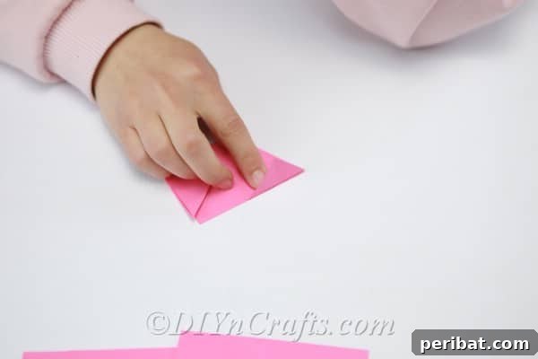 Pink paper in the process of being folded to refine the petal shape, showing an internal fold