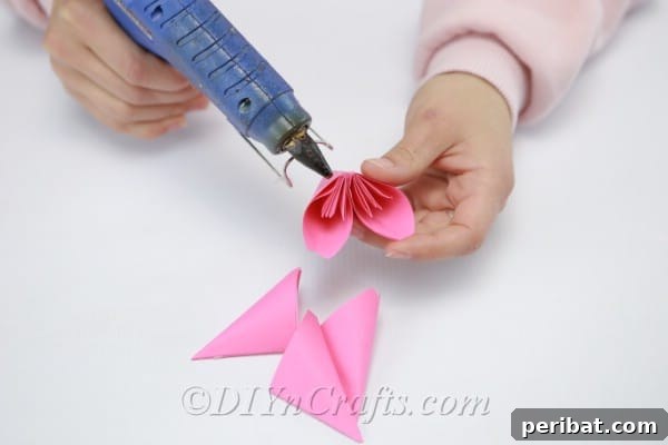 Assembling additional leaves onto a pink paper flower, building its full and layered appearance