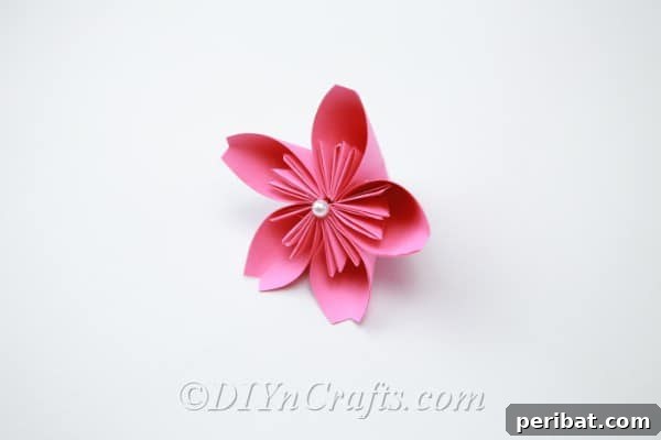 A pink paper flower adorned with a small pearl glued in its center, adding a touch of elegance