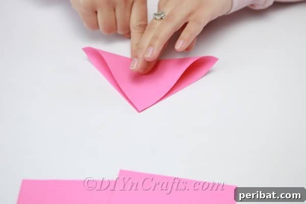 Pink paper square being folded in half diagonally to form a neat triangle