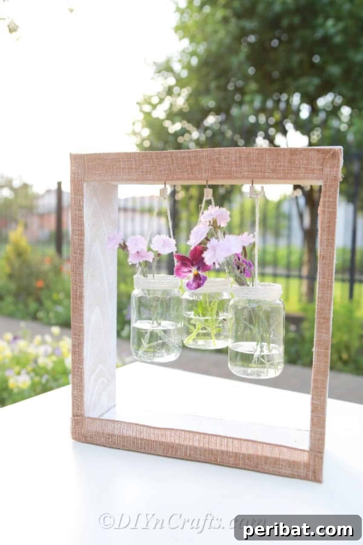 A close-up view of a glass jar vase hanging within a weathered wooden box, adorned with vibrant purple flowers, showcasing the intricate detail and charm of the DIY project.