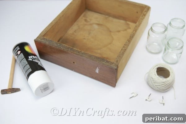 Old drawer and supplies for a DIY hanging vase project, including glass jars, twine, and hooks, laid out on a rustic wooden surface.