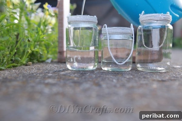 Three glass jars with twine meticulously wrapped around their tops, preparing them for suspension, sitting next to a rustic wooden frame.