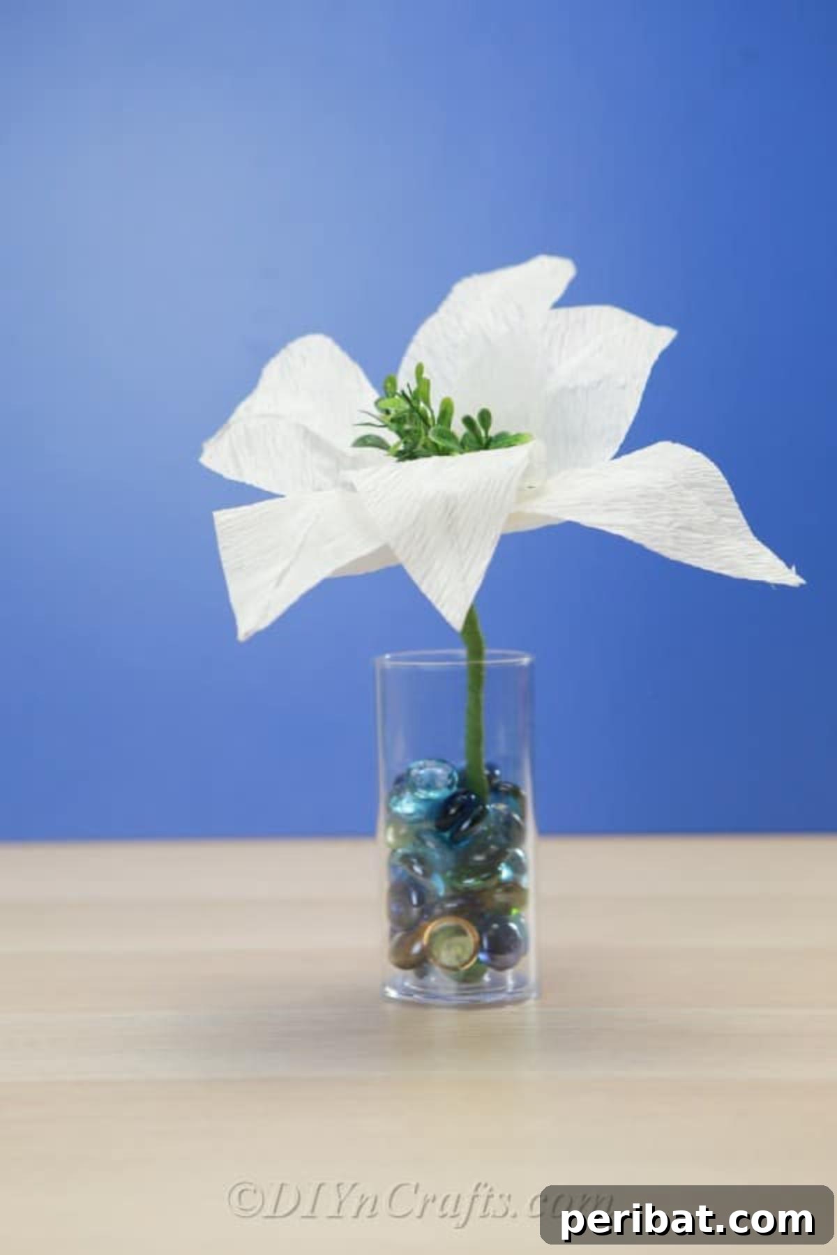 Vibrant tissue paper flower arranged in a jar with decorative marbles, showcasing a homemade touch.