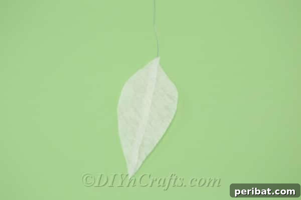 A tissue paper triangle is being carefully cut with scissors into a distinct leaf shape, demonstrating precision in crafting.
