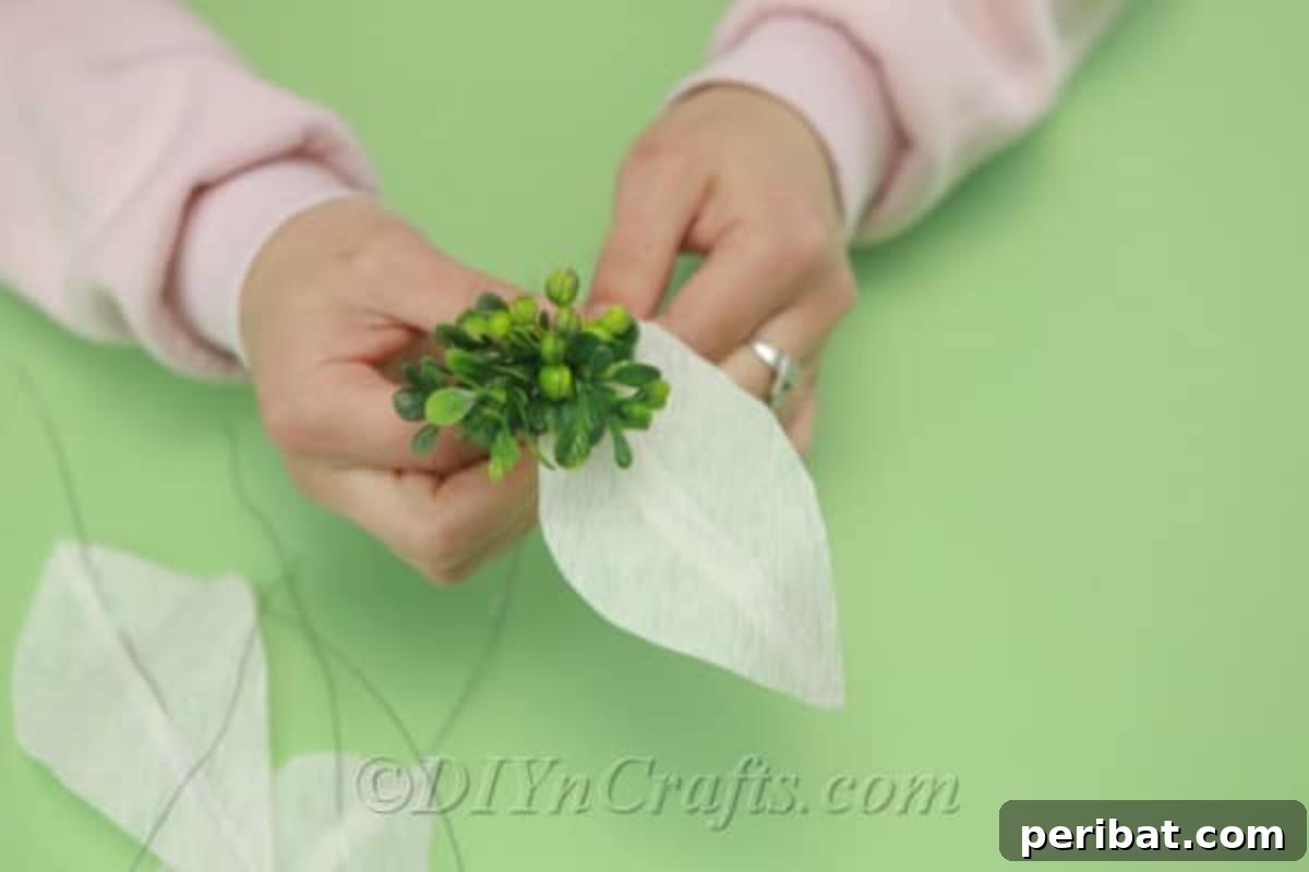 Multiple green tissue paper leaves are being attached to a central white tissue paper flower, simulating natural greenery.