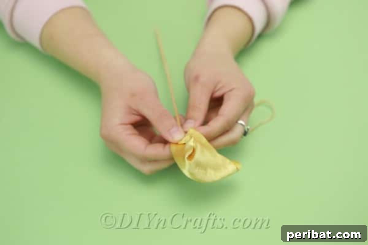 A wooden dowel is being carefully wrapped with a yellow satin fabric, forming the initial shape of a tulip.