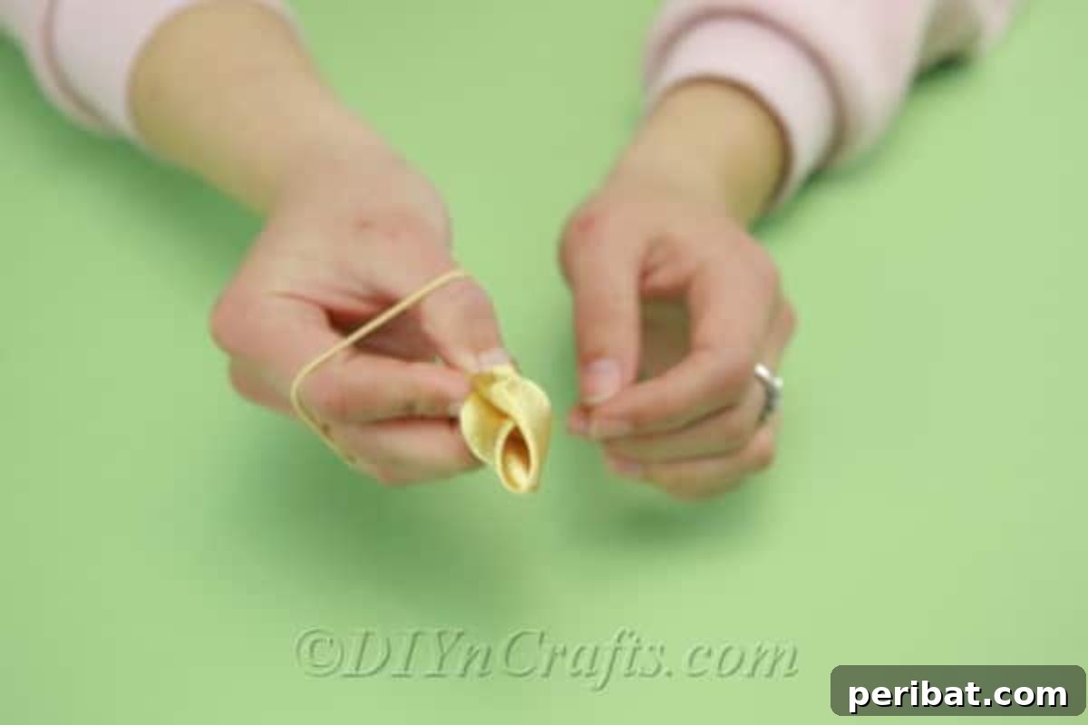 A crafter's hands expertly making a distinct tulip shape from vibrant yellow satin fabric around a central rod.