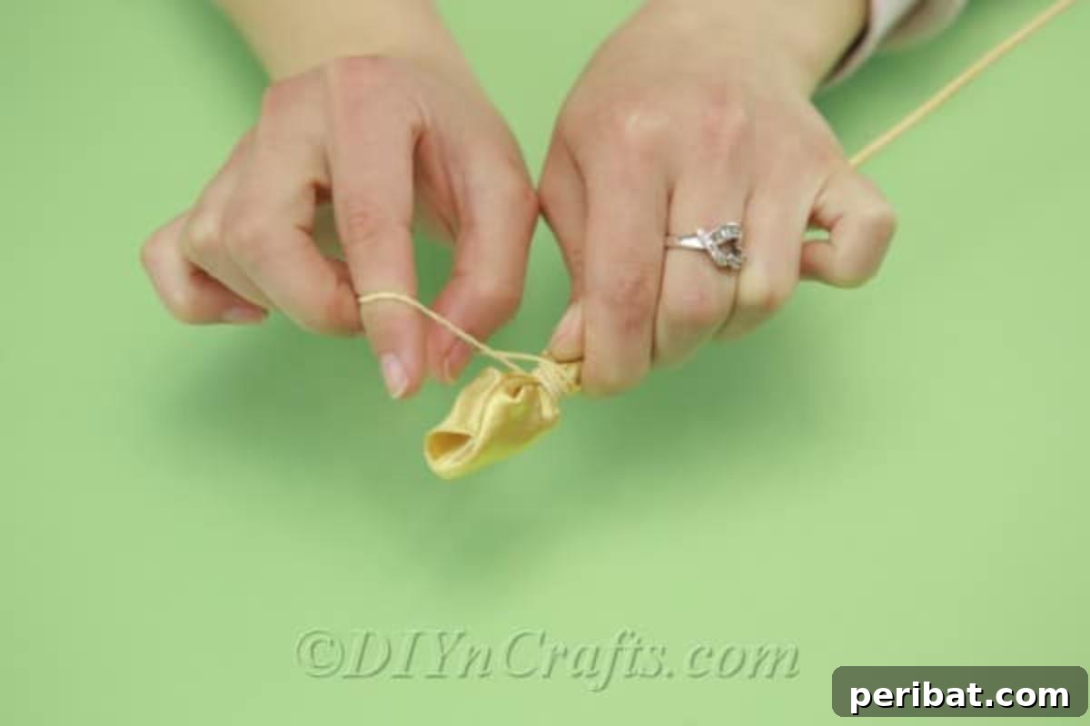 A yellow satin tulip is being secured at its base with a rubber band wrapped around a wooden dowel, holding the petals in place.