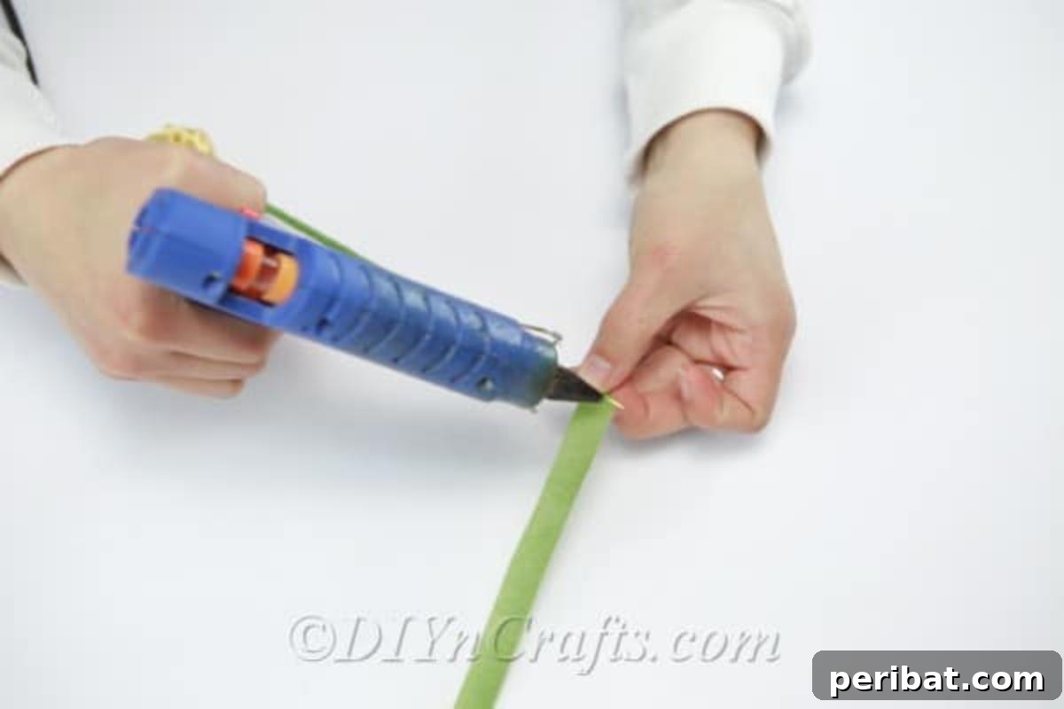 The process of completely covering a wooden dowel in green ribbon, transforming it into a realistic flower stem.