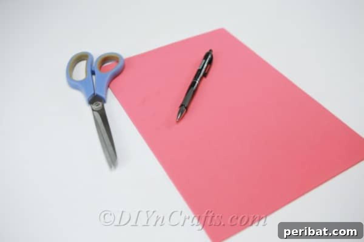 A clear flat lay of craft supplies needed for making a foam flower: a sheet of pink craft foam, a hot glue gun, scissors, and a pencil.