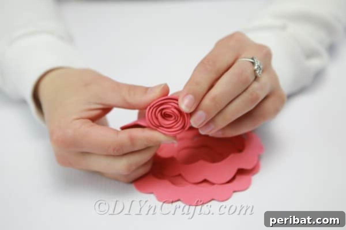 A long strip of craft foam, cut in a wavy spiral, is being rolled up from the outside edge to create a flower shape.