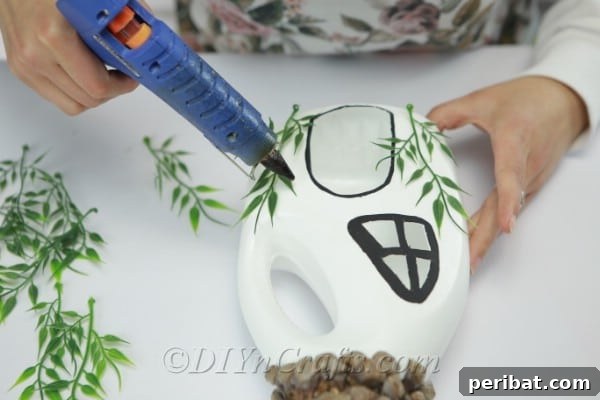 Gluing branches and flowers onto the front of a fairy house for aesthetic appeal and whimsy