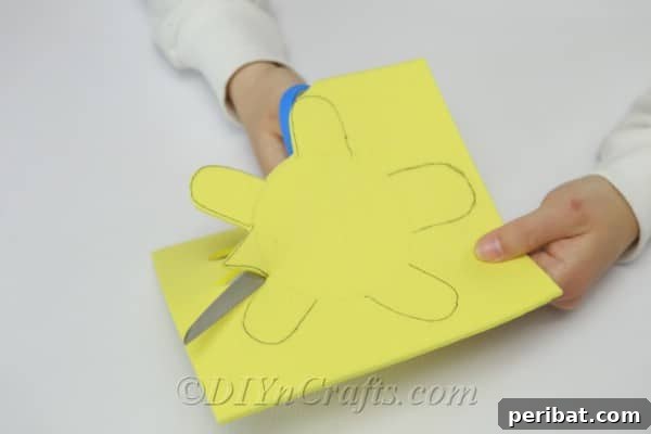 Child's hands carefully cutting out the turtle shape from the yellow craft foam using scissors.