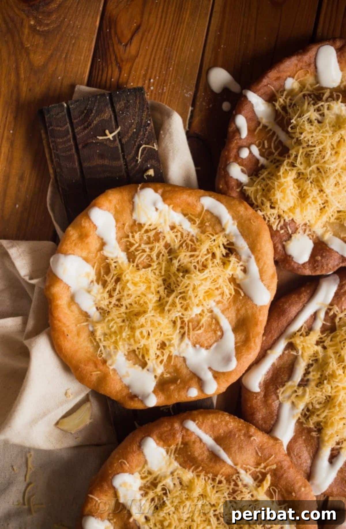 Hungarian langos topped with shredded cheese and sour cream, glistening and golden