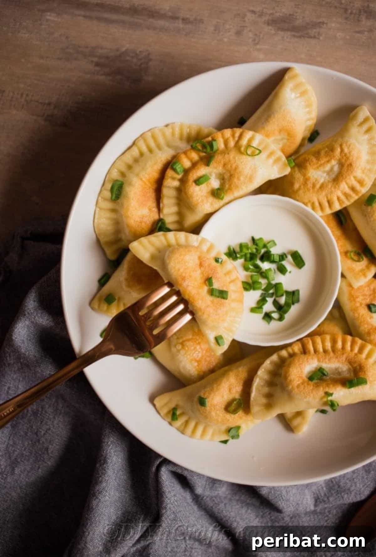 Effortless Potato Pierogi Delight 4 A freshly cooked potato pierogi speared on a fork, dipped in sour cream and ready to be enjoyed.