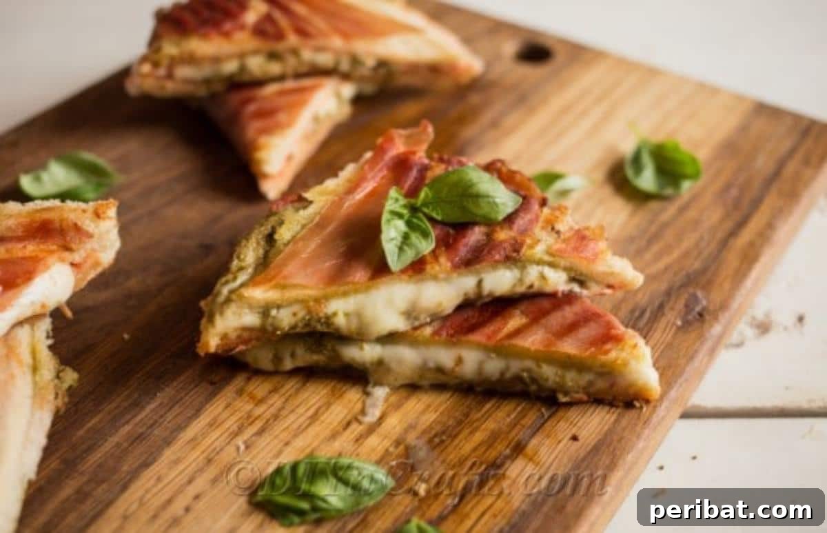 Pesto Perfection Grilled Cheese 2 Gourmet Pesto grilled cheese with crispy prosciutto on top, golden brown and sliced diagonally, ready to serve