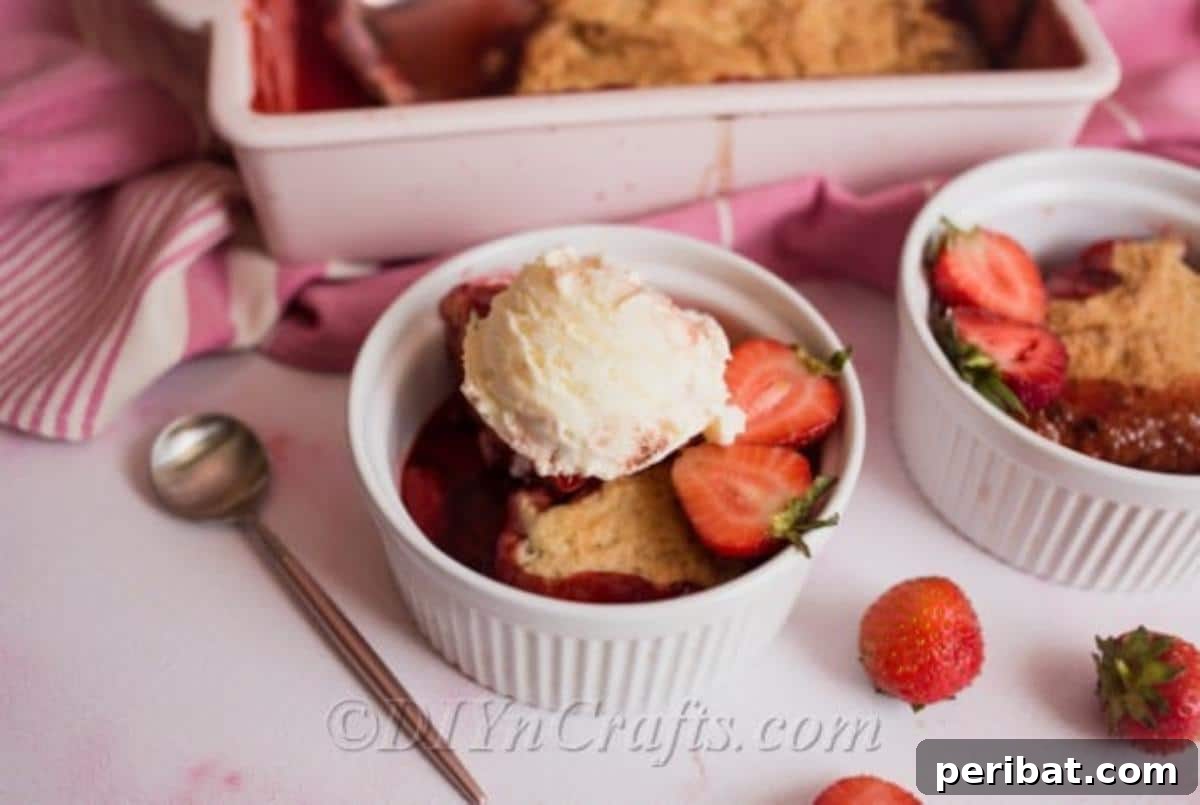 Close-up of strawberry cobbler in a dish with a scoop of vanilla ice cream and a spoon.