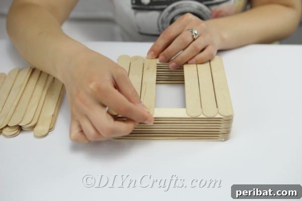 Start constructing the floor of the bird feeder by gluing sticks across the top of the walls.
