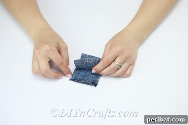 Fold the denim strip multiple times lengthwise to create layers for cutting.