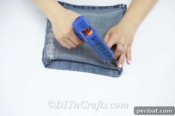 Apply hot glue to one end of the denim pant leg and fold it to create a sealed base.