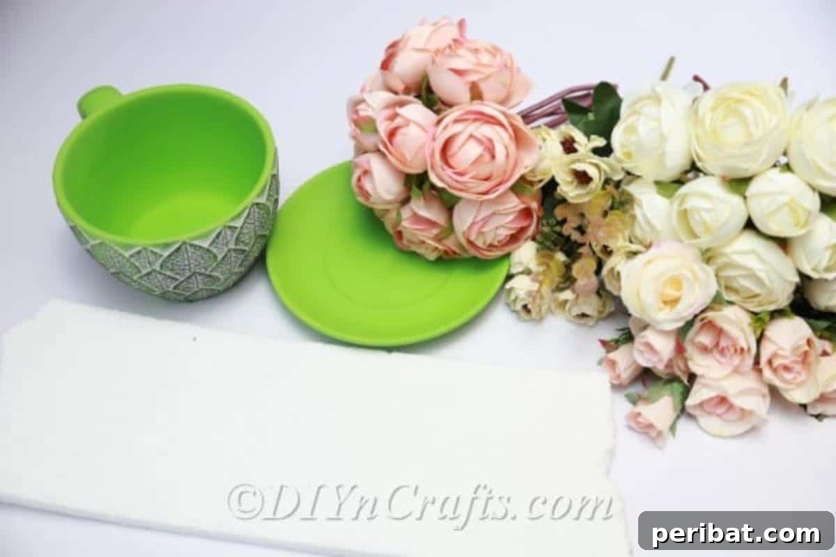 Floral Magic in a Teacup 4 Arrangement of craft supplies including faux flowers, a teacup, Styrofoam, and cutting tools laid out on a clean surface.