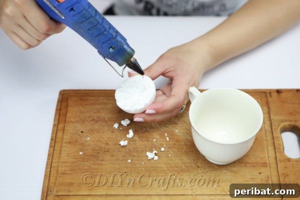 Apply hot glue to the flat side of one of the Styrofoam ball halves before placing it into the cup.