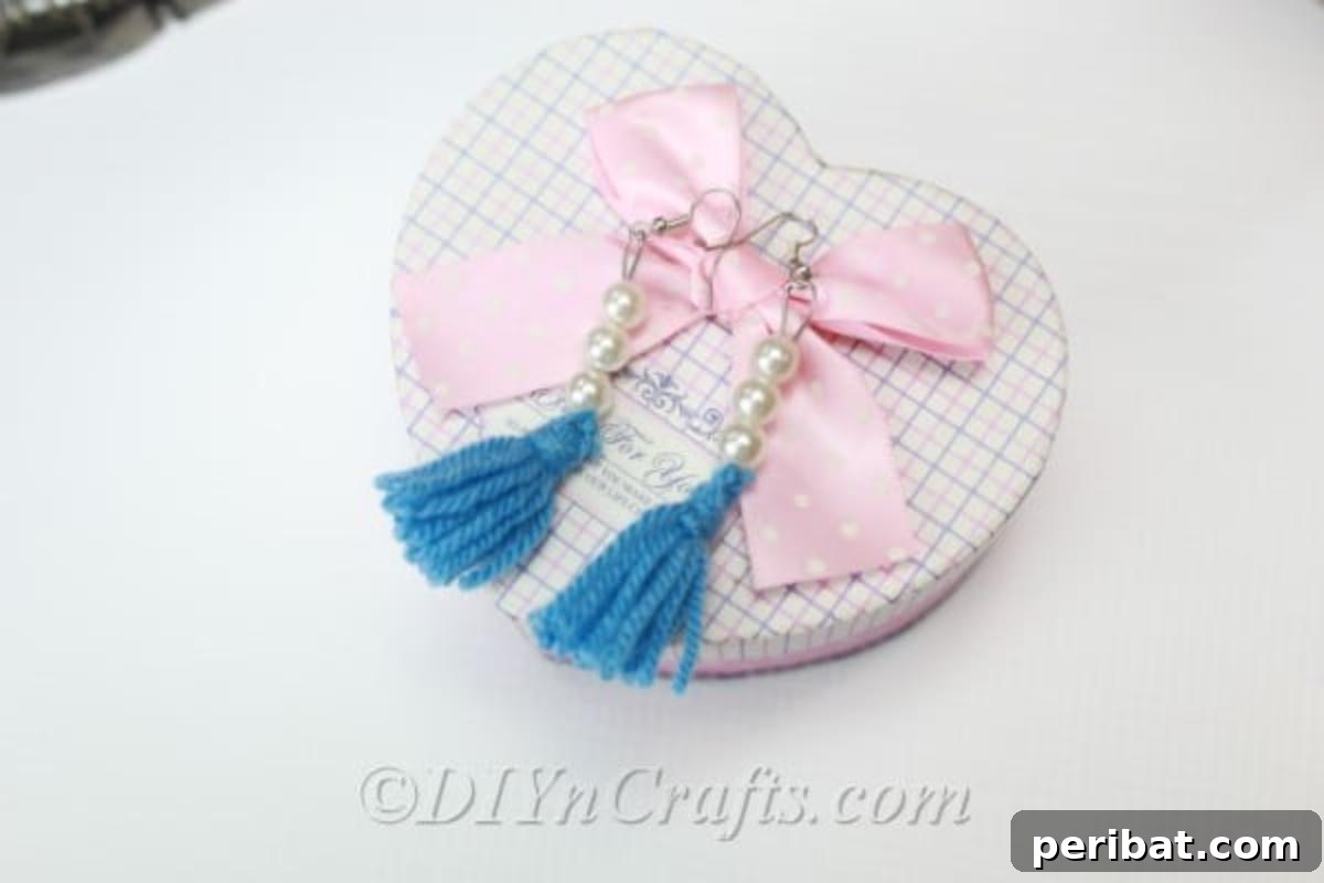 Create Your Own Trendy Yarn Tassel Earrings 3 Two elegant yarn tassel earrings, one navy and one mustard yellow, carefully displayed on a decorative heart-shaped box.