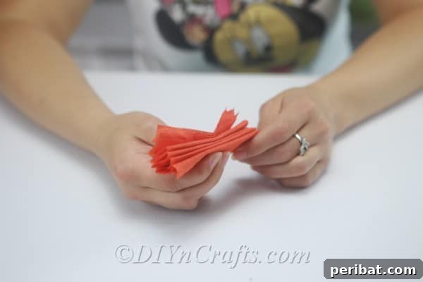 Carefully pinching the center of the accordion-folded tissue paper to create a bow-tie shape.