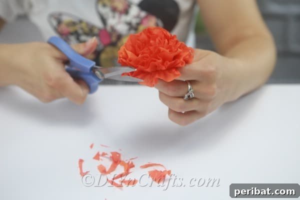 Making small adjustments by trimming the edges of the tissue paper flower to ensure a uniform and neat appearance.