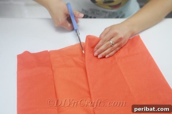 The initial step of folding a large piece of tissue paper multiple times to prepare for cutting.