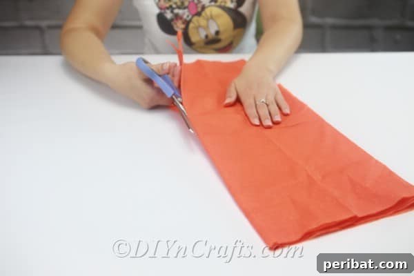 Carefully cutting along the folded edges of the tissue paper to create multiple long strips.