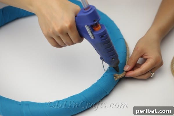 Coastal Elegance: Craft Your Perfect Summer Wreath 13 Carefully hot glue the thin rope onto the outer edge of the fabric-covered wreath.