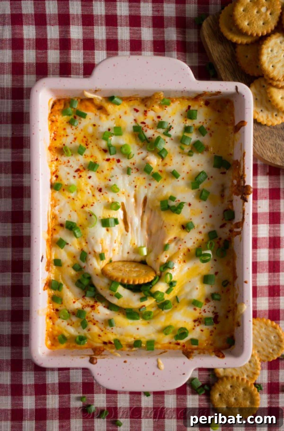 Quick & Creamy Buffalo Chicken Dip 6 Close-up of a Ritz cracker being dipped into a warm, creamy dish of Easy Buffalo Chicken Dip, ready to be enjoyed