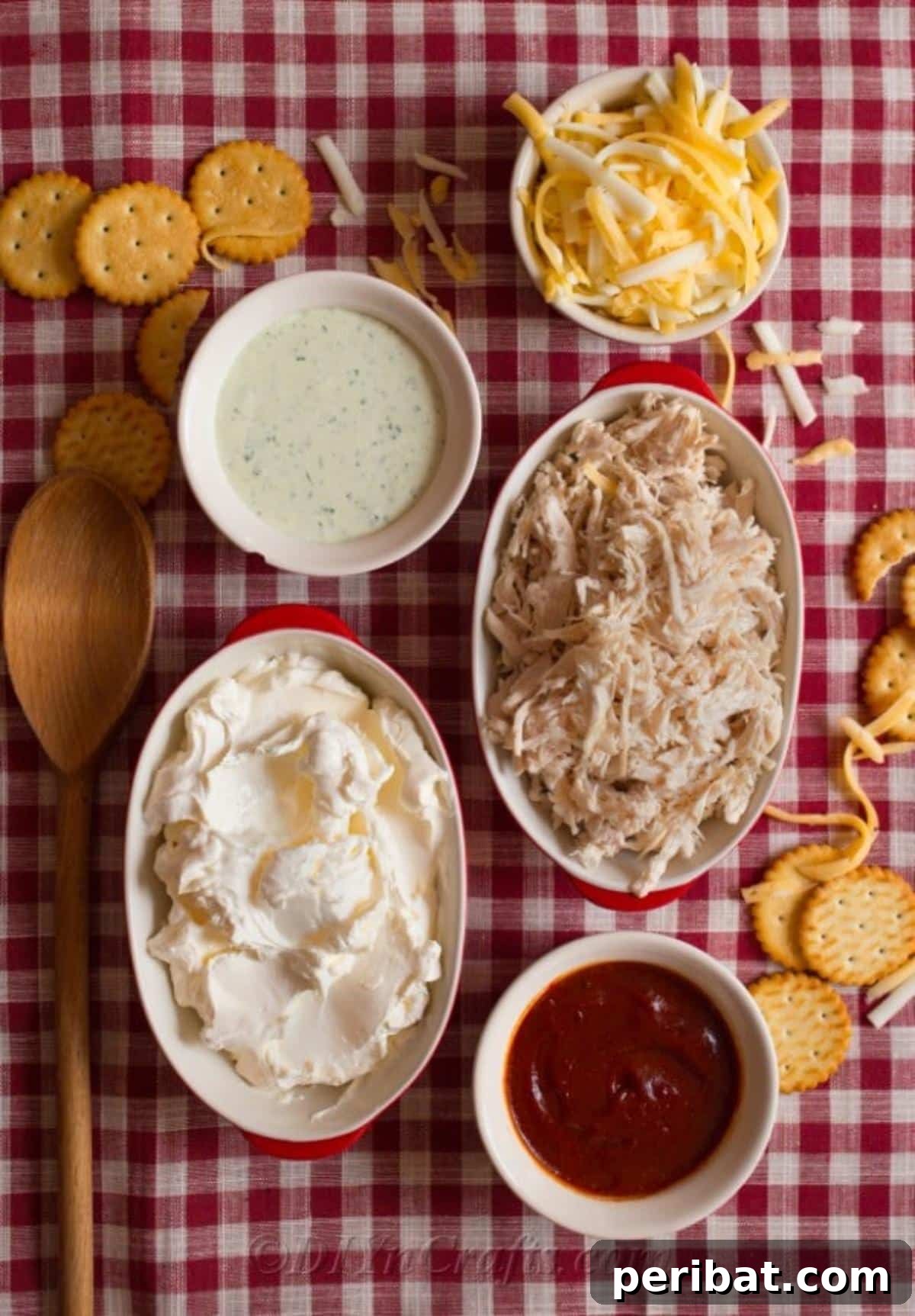 Quick & Creamy Buffalo Chicken Dip 7 Fresh ingredients for easy buffalo chicken dip, including cream cheese, cooked chicken, hot sauce, blue cheese dressing, and cheddar cheese, arranged on a red and white checkered cloth