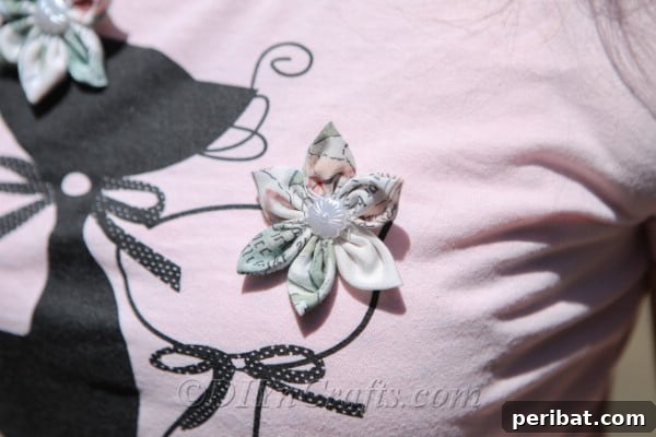 A simple yet elegant fabric flower, featuring a delicate pearl center, pinned to a t-shirt as a chic accessory.